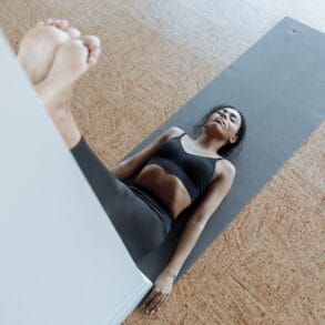 Vrouw ligt op een yogamat met haar benen omhoog tegen de muur, een rustige houding voor het slapengaan