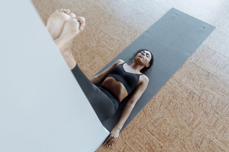 Vrouw ligt op een yogamat met haar benen omhoog tegen de muur, een rustige houding voor het slapengaan